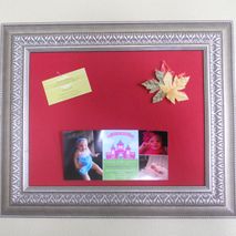 Framed cork bulletin board covered in red fabric.